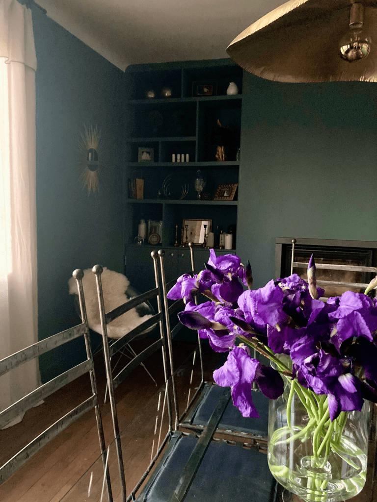 Table à manger en verre de Blois et chaises en métal, armoire sombre sur mesure Loire et Cher, lampes Mesland vintage, miroirs dorés vintage et modernes, fleur violette au centre de la table 