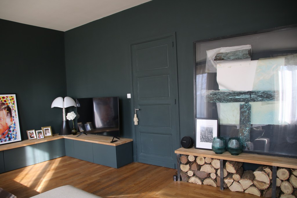 Rangement sur mesure à Blois, tableau artistique avec rangement pour bois en dessus, coin télé en Loir et Cher,  lampe avec style original, Mur couleur sombre entre bleu et vert,  