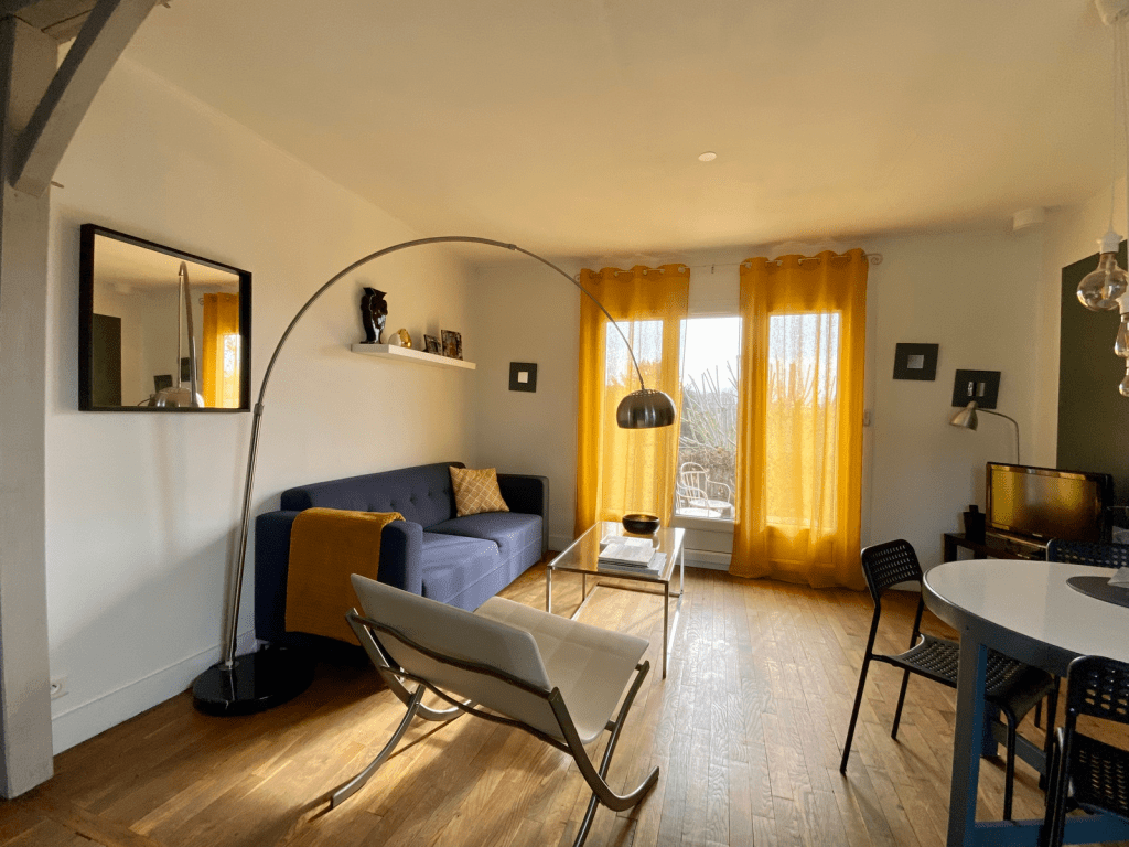 Salon au couleur bleu blanc et jaune à Blois, table à manger ronde avec chaise en metal noir en Loir et Cher, grand miroir noir avec lampadaire style vintage à Mesland, fenêtre avec rideau jaune, 